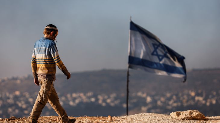 A Jewish settler teenager walks by an Israeli flag in Givat Eviatar, a new Israeli settler outpost, near the Palestinian village of Beita in the Israeli-occupied West Bank June 23, 2021.