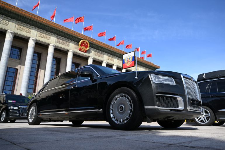 Vladimir Putin's Aurus outside the Great Hall of the Poeple in Beijing. There is a presidential pennant on the car's front right wing. The vehicle is black with a large grille at the front.