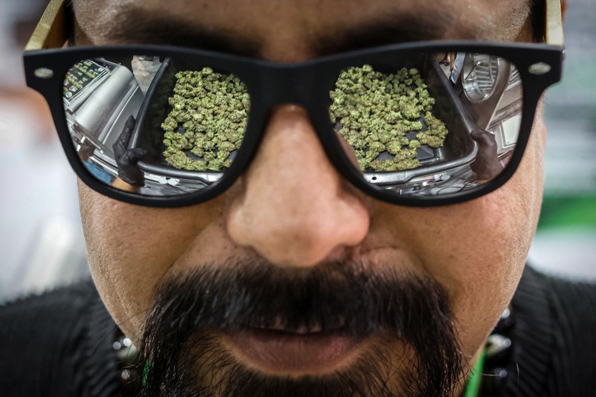 Cannabis buds are reflected on a man's sunglasses, as he demonstrates how a trimmer machine works during a cannabis industry expo in Bangkok