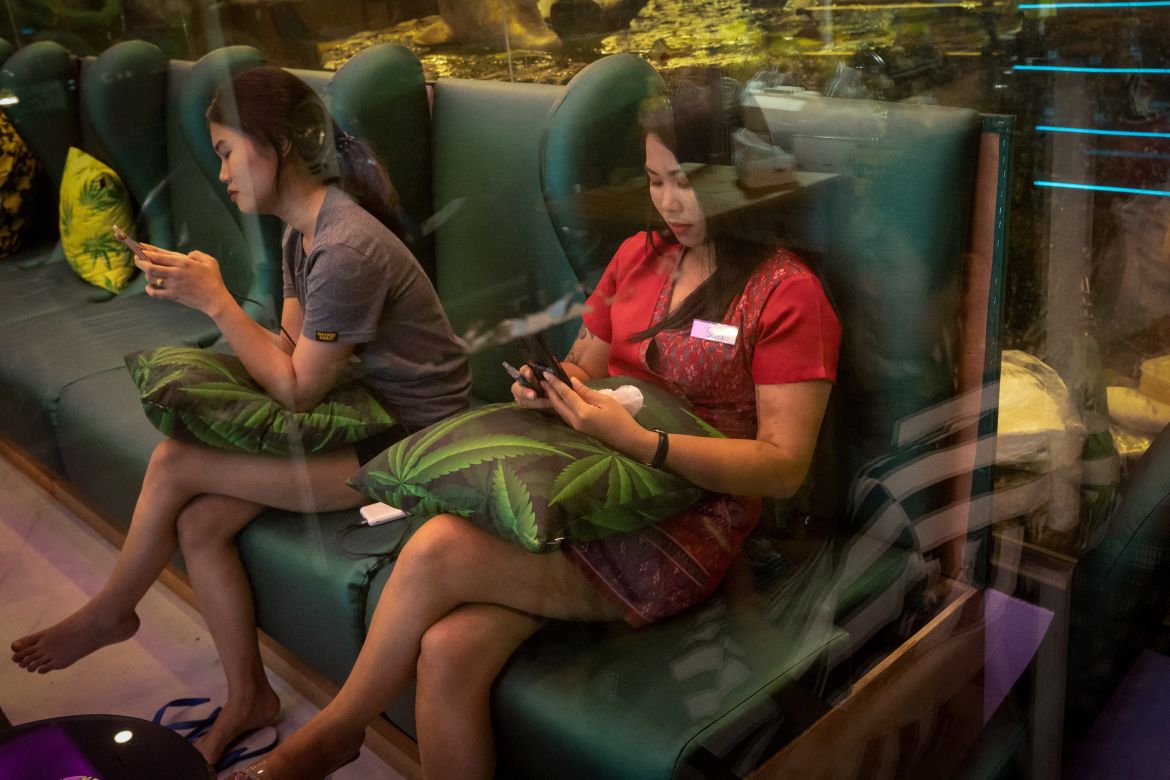 Women wait for customers in a massage shop with cannabis-themed decorations in Phuket, Thailand