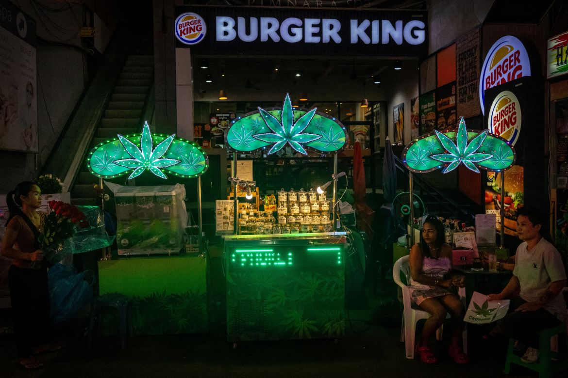 People sit near stalls selling cannabis on a street in Phuket, Thailand