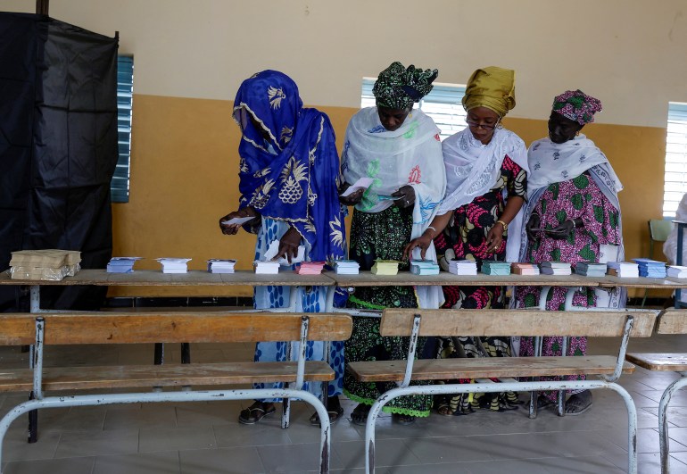An election worker helps women to collect voting ballots at the polling station at Ndiaganiao in Mbour