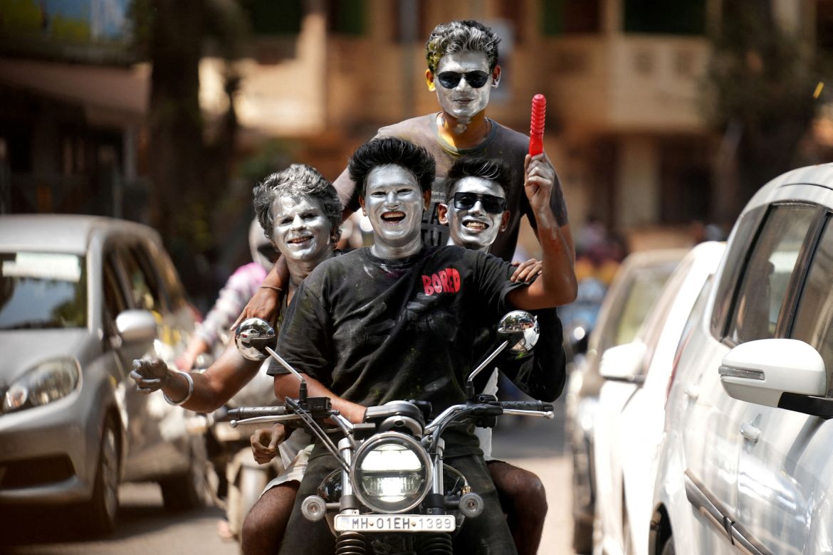 Boys with their faces painted in silver ride a motorbike during Holi celebrations in Mumbai