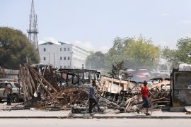 People walk past remains of vehicles near the presidential palace, after they were set on fire by gangs, as violence spreads and armed gangs expand their control over the capital, in Port-au-Prince, Haiti [Ralph Tedy Erol/Reuters]