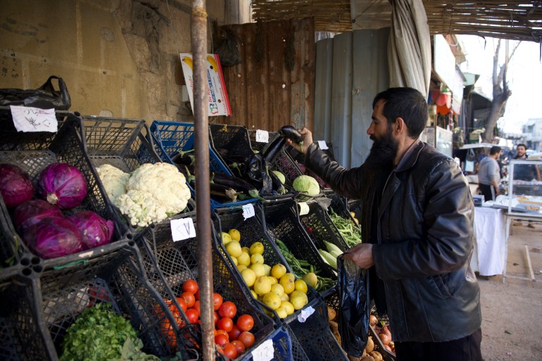 Khalid, a gentle, bearded man, picks out vegetables from a simple stand in the market