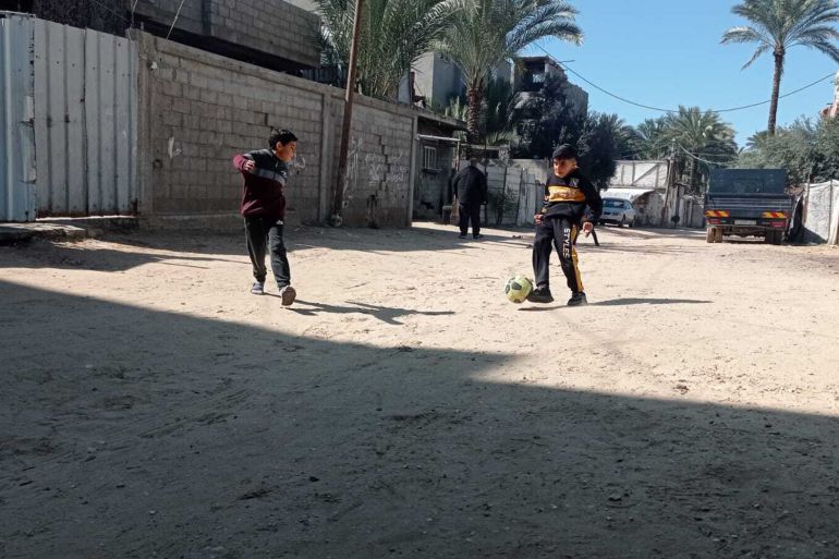 A group of children play football in the street under the shadow of drones in Deir al-Balah, Gaza [Abubaker Abed/Al Jazeera]