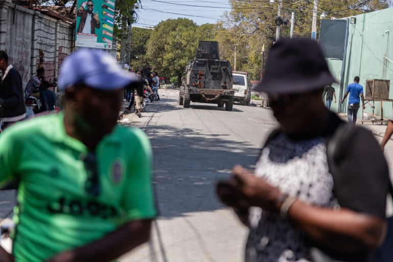 An armoured police tank drives by people in Port-au-Prince