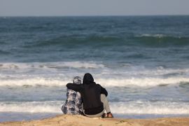 A couple watches the waves at the beach near a makeshift tent camp for displaced Palestinians in Rafah in the southern Gaza Strip, on January 24, 2024 [AFP]