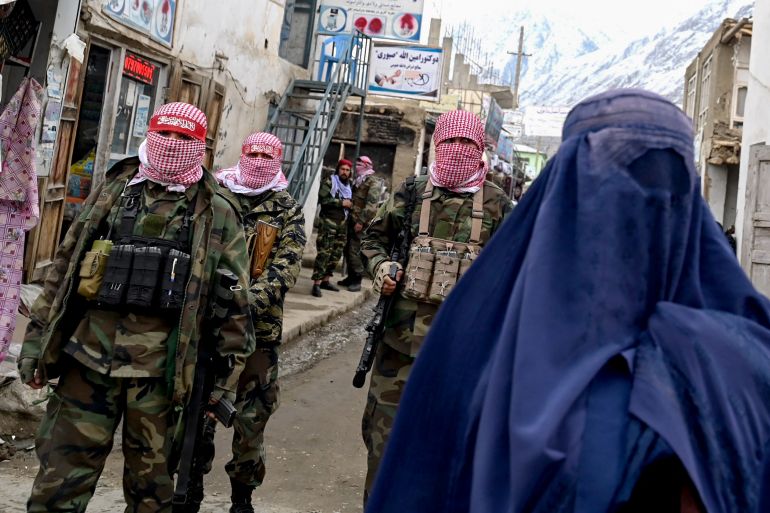 Taliban security personnel stand guard as an Afghan burqa-clad woman walks along a street at a market in the Baharak district of Badakhshan province