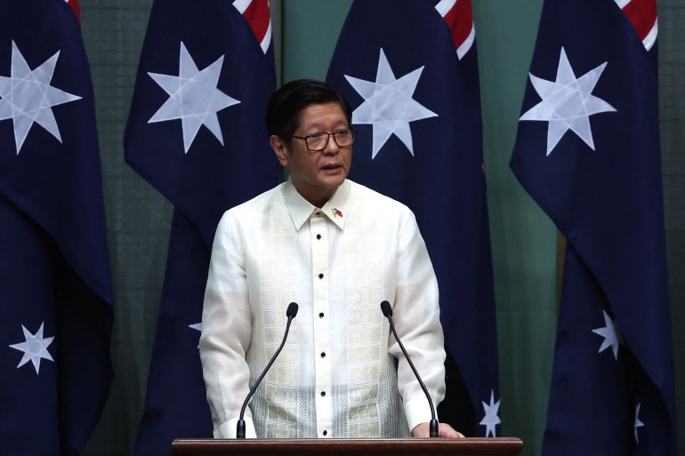 a man in white shirt speaks in front of Australian flags