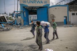 children carry a bag of flour past a destroyed UNRWA building
