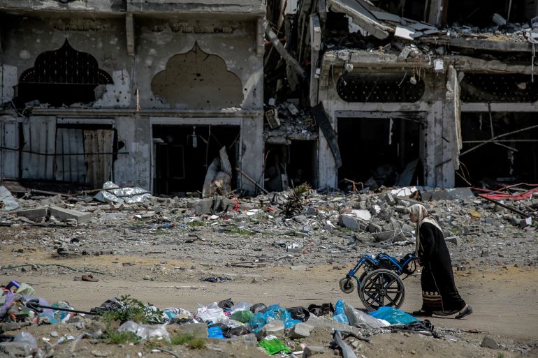 A woman pushes a wheelchair next to destroyed buildings in the northern Gaza Strip on March 21, 2024, amid the ongoing violence between Israel and the Palestinian Hamas movement. (Photo by AFP)