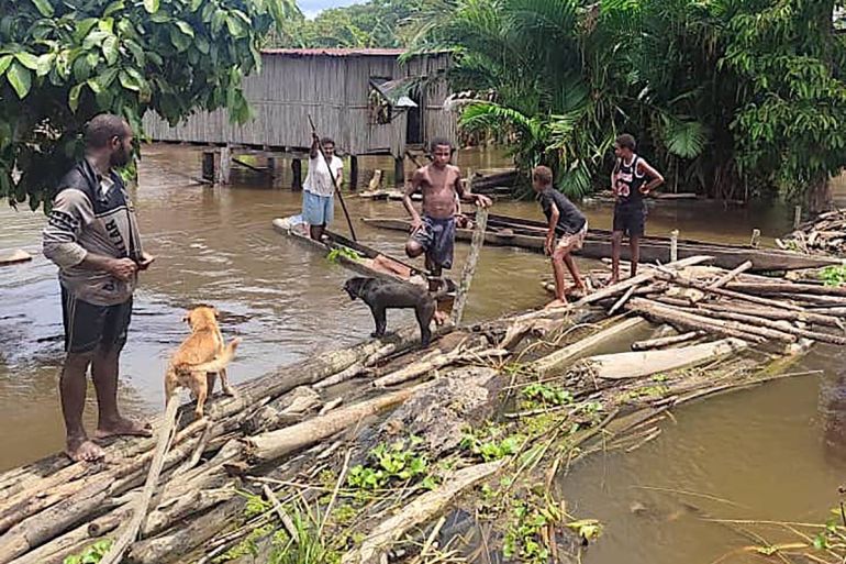 This photo released by the Papua New Guinea Police and received by AFP on March 25, 2024 shows locals on a makeshift bridge in the flooded Angriman Village in Angoram District, East Sepik, Papua New Guinea. - At least five people were killed and an estimated 1,000 homes destroyed when a magnitude 6.9 earthquake rocked Papua New Guinea, officials said March 25 as disaster crews poured into the region. Dozens of villages nestled on the banks of the country's Sepik River were already battling soaking floods when the quake struck early March 24. (Photo by Handout / PAPUA NEW GUINEA POLICE / AFP) / RESTRICTED TO EDITORIAL USE - MANDATORY CREDIT "AFP PHOTO / PAPUA NEW GUINEA POLICE " - NO MARKETING NO ADVERTISING CAMPAIGNS - DISTRIBUTED AS A SERVICE TO CLIENTS - RESTRICTED TO EDITORIAL USE - MANDATORY CREDIT "AFP PHOTO / PAPUA NEW GUINEA POLICE " - NO MARKETING NO ADVERTISING CAMPAIGNS - DISTRIBUTED AS A SERVICE TO CLIENTS /