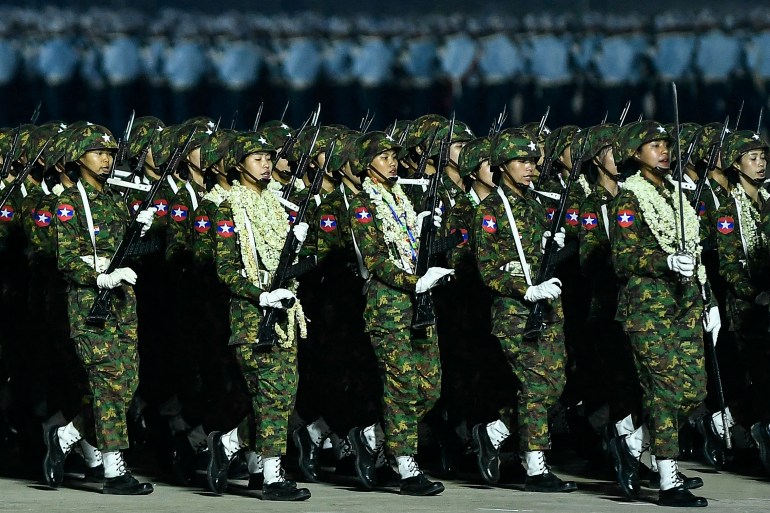 Myanmar women soldiers march in their parade. They are carrying weapons and some have multiple flower garlands around their necks
