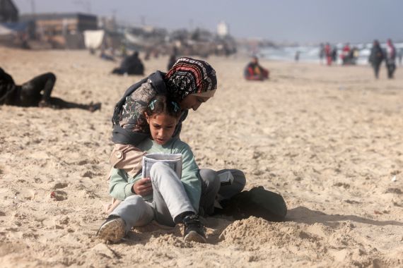 A Palestinian woman and a girl sit along a beach adjoining a makeshift camp for displaced people in Rafah in the southern Gaza Strip on March 30