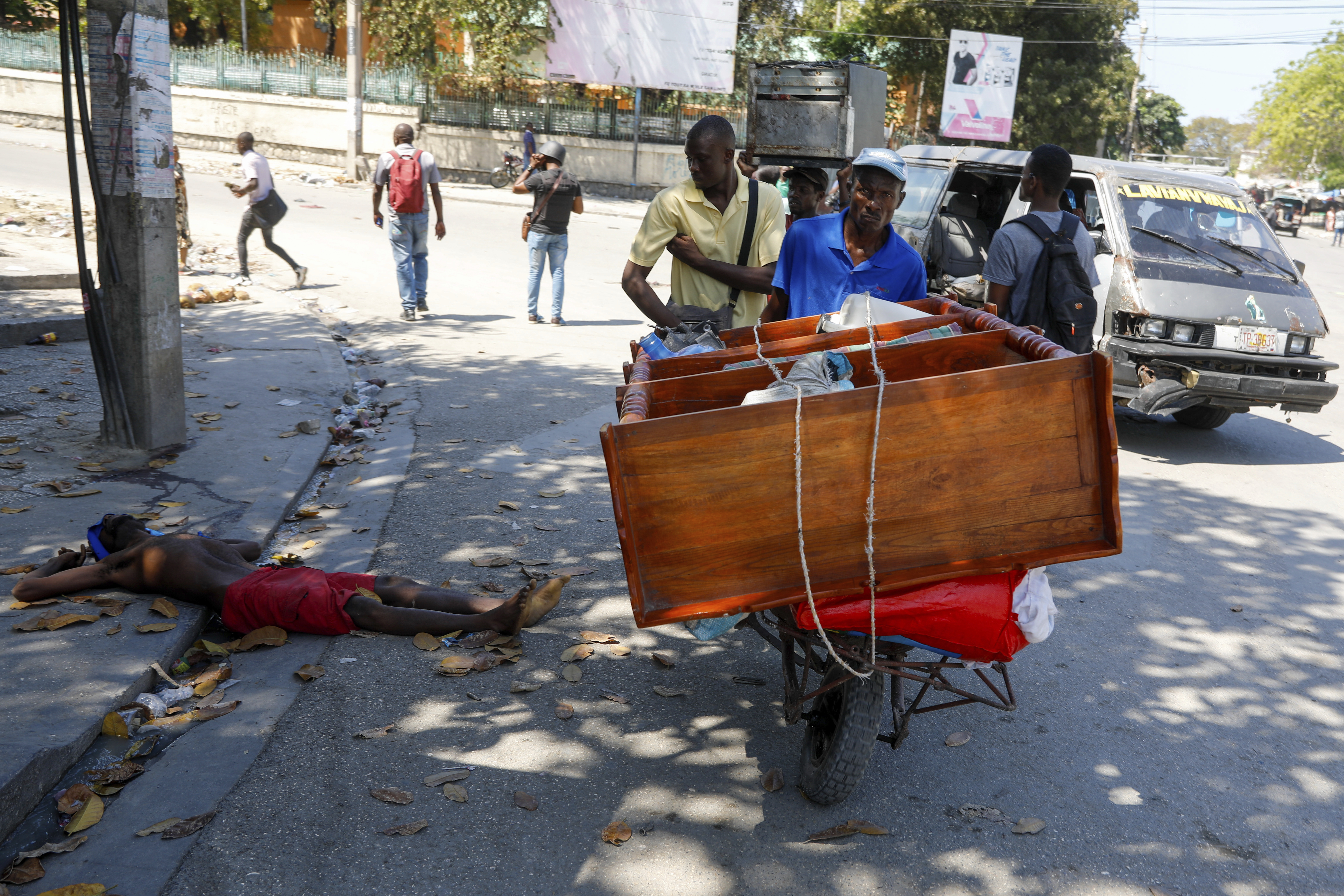 A man pushes a cart past the body of a man shot by unidentified assailants