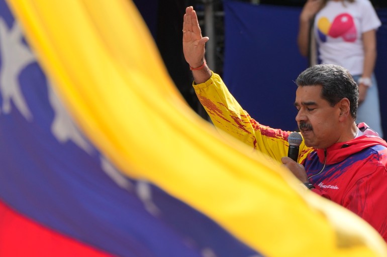 Nicolas Maduro waves behind a Venezuelan flag.