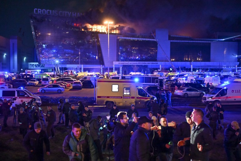 People outside the Crocus Concert Hall after the attack. Flames are rising from the top of the building. Emergency vehicles are in the car park below.