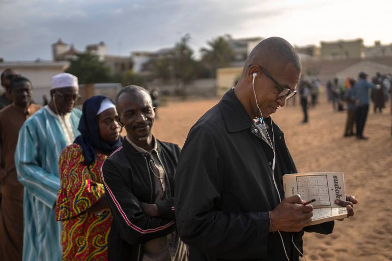 A man solves a sudoko riddle as he waits in line to cast his votes outside a polling station during the presidential elections, in Dakar, Senegal, Sunday, March 24, 2024. (AP Photo/Mosa'ab Elshamy)