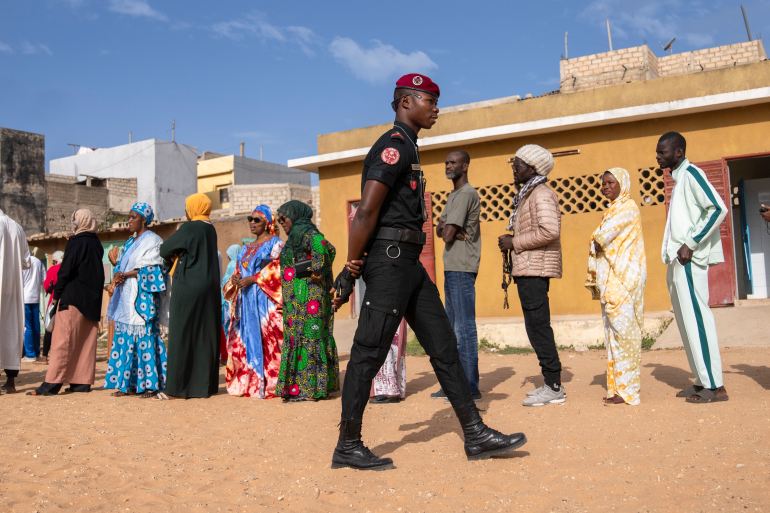 A member of security forces stands guard as people wait to cast their votes outside a polling station during the presidential elections, in Dakar, Senegal, Sunday, March 24
