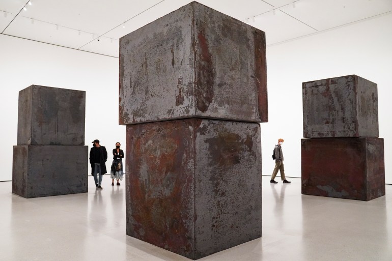 People walking around the Richard Serra work 'Equal'. They are dwarfed by the towering rusted steel blocks 