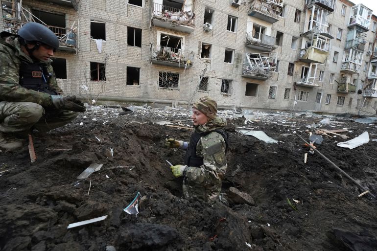 Ukrainian police inspecting a large crater hit by a Russian missile. A damaged apartment building is behind them.