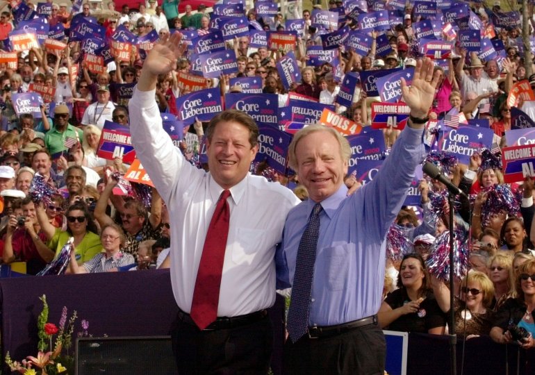 Standing in front of a crowd of supporters, Al Gore and Joe Lieberman wave.