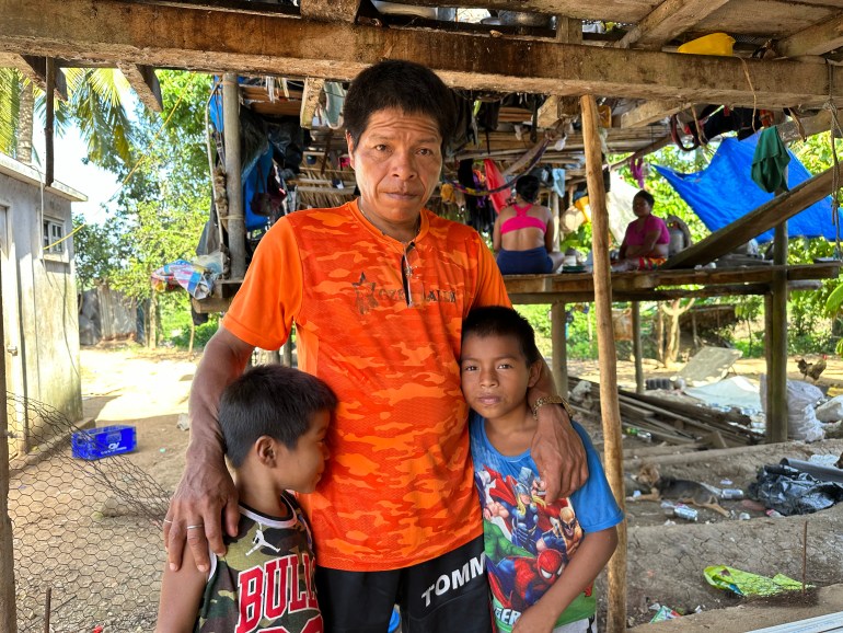 A man in an orange T-shirt poses for a photo, with his two children by his side.