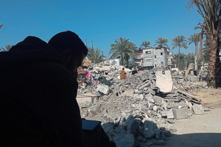 Hamza El Outy watches football highlights next to the rubble of his destroyed house near Deir al-Balah, Gaza [Abubaker Abed/Al Jazeera]
