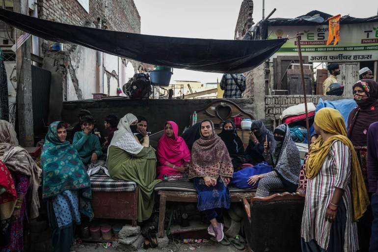 Shabana Hasan, 41, wife of Wakeel Hasan, 45, and relatives sit on a wrecked bed outside their demolished house to protest the demolition. [Md Meharban/Al Jazeera]