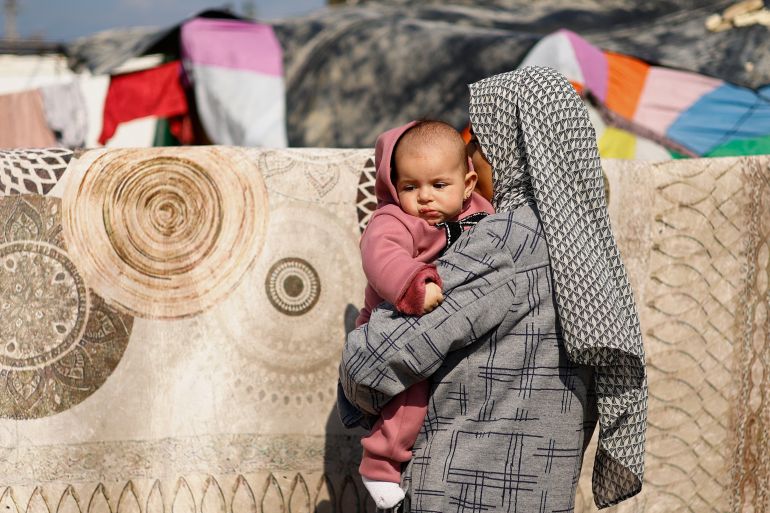 A woman holds a baby, as displaced Palestinians, who fled their houses due to Israeli strikes, take shelter in a tent camp amid the ongoing conflict between Israel and Hamas, in Rafah in the southern Gaza Strip, February 6, 2024
