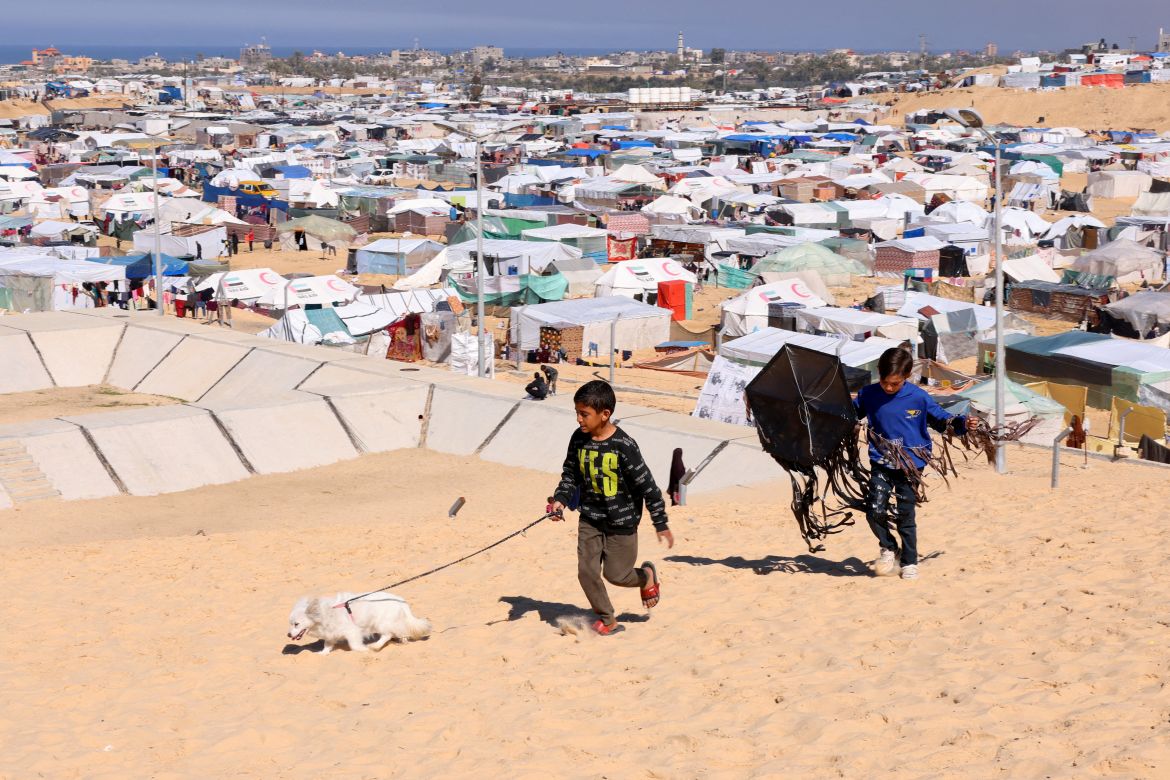 Children walk with a dog, as displaced Palestinians, who fled their houses due to Israeli strikes, take shelter in a tent camp, amid the ongoing conflict between Israel and the Palestinian Islamist group Hamas, at the border with Egypt, in Rafah in the southern Gaza Strip, February 8