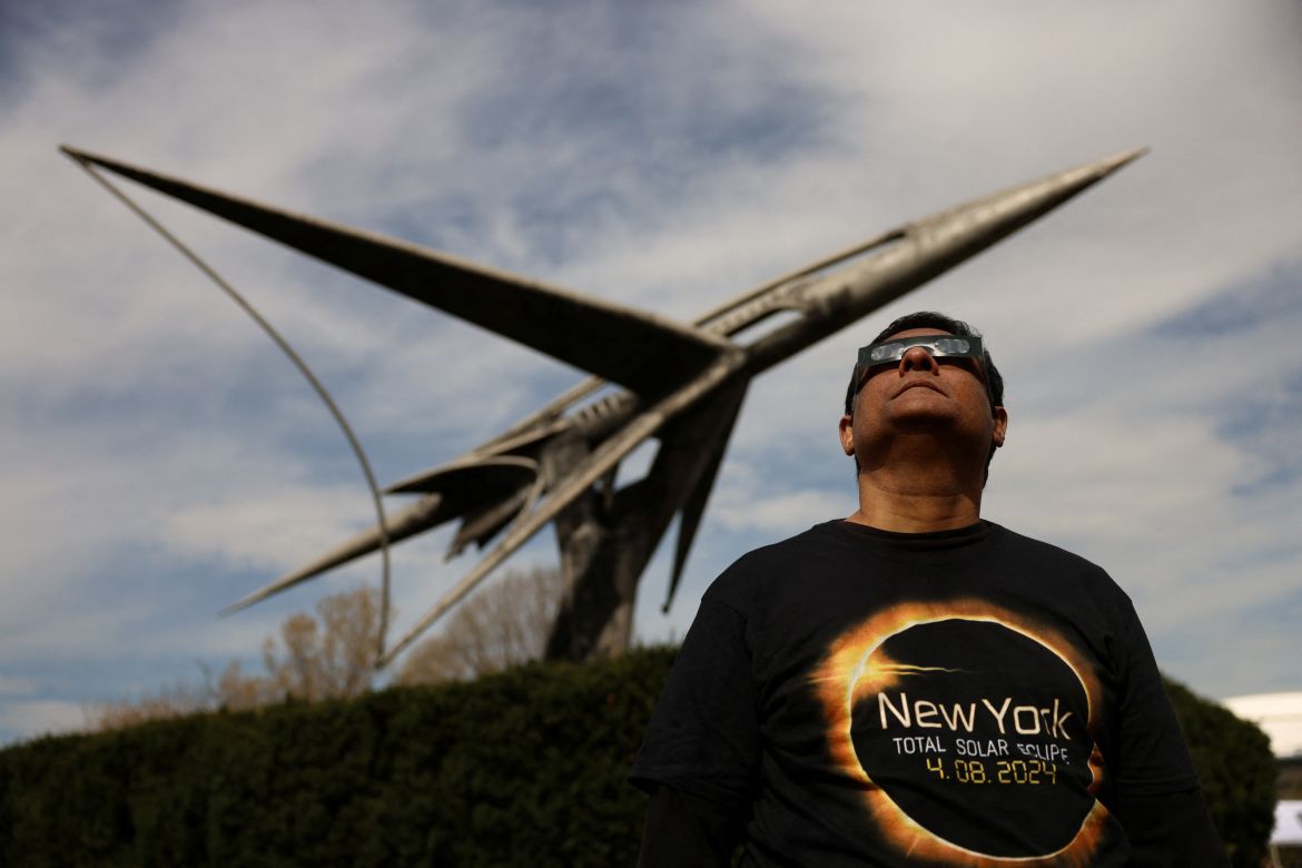 Standing in front of a jet on display, a man looks through glasses at the eclipse.