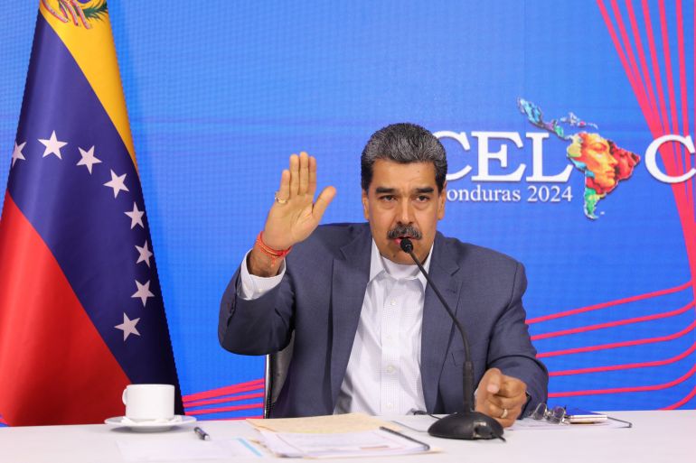 Nicolas Maduro lifts his hand and speaks into a microphone.