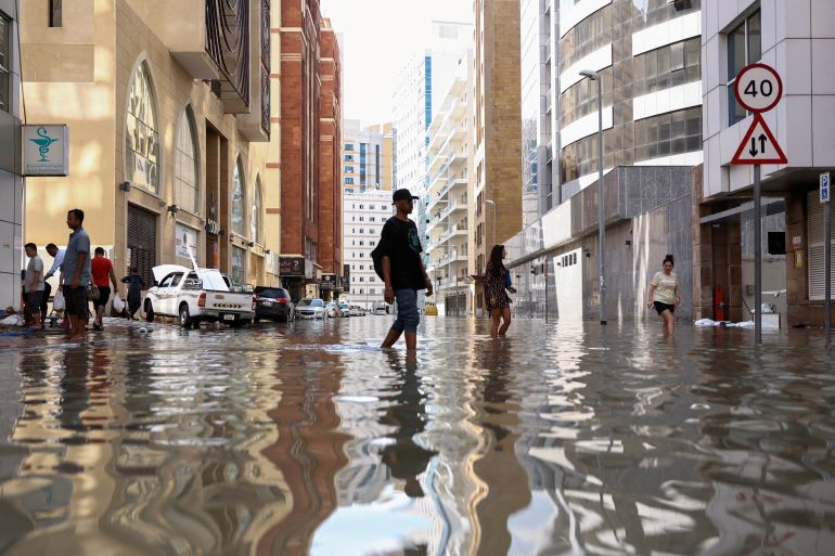 People walk through flood water caused by heavy rains, in Dubai