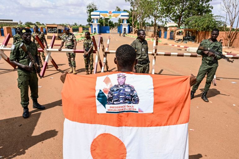 A supporter of the Niger's National Council for the Safeguard of the Homeland (CNSP) wears a Niger's flag with a picture of Niger's new military ruler, General Abdourahamane Tiani, as they demonstrate ouside the Niger and French airbases in Niamey on August 27, 2023. (Photo by AFP)