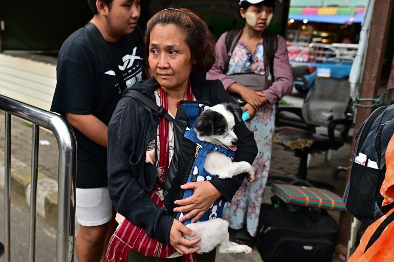 A woman from Myawaddy carrying her dog as she waits to cross into Thailand. The dog is black and white and wearing a blue harness