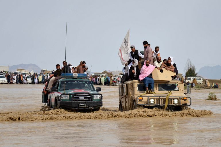 Afghan men sit atop of military vehicles amid flooding