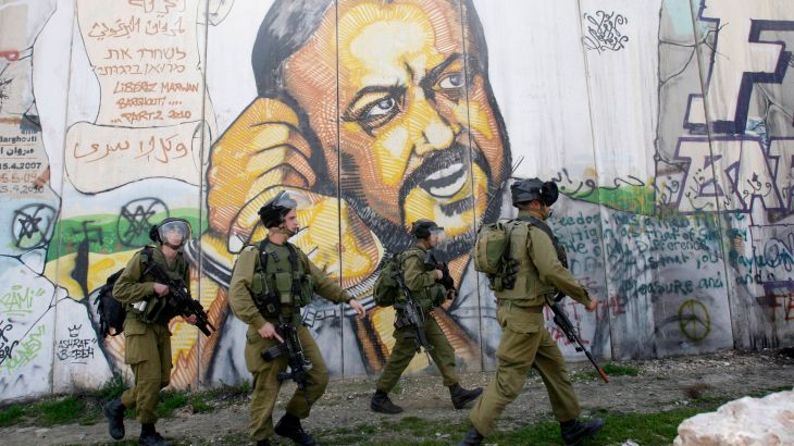 In the background of part of Israel's separation barrier with portrait of jailed Fatah leader Marwan Barghouti, Israeli soldiers patrol at Kalandia checkpoint between Jerusalem and the West Bank city of Ramallah,