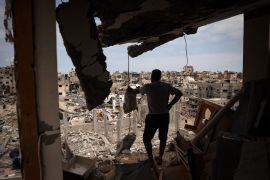 A Palestinian man looks at a ravaged neighbourhood from a destroyed apartment in Khan Younis in southern Gaza [AFP]