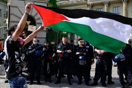 A demonstrator holds up the Palestinian flag as police block the entrance of Humboldt University following a pro-Palestinian sit-in in Berlin, Germany. [John Macdiugall/AFP]