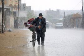 A displaced Palestinian man pushes a bycicle bearing his belongings in the rain in Rafah in the southern Gaza Strip following an evacuation order by the Israeli army [AFP]