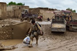 A man carries his belongings as he walks through a muddy street following a flash flood in Afghanistan&#039;s Baghlan province [AFP]