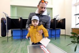 A voter with child prepares to cast a ballot into an urn during the first round of Lithuania&#039;s presidential election at a polling station in Vilnius [Petras Malukas/AFP]