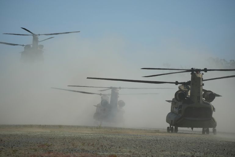 US army helicopters in clouds of dust as they take off from Ilocos Norte province during the Balikatan exercises. There are three helicopters. The one the farthest away is taking off